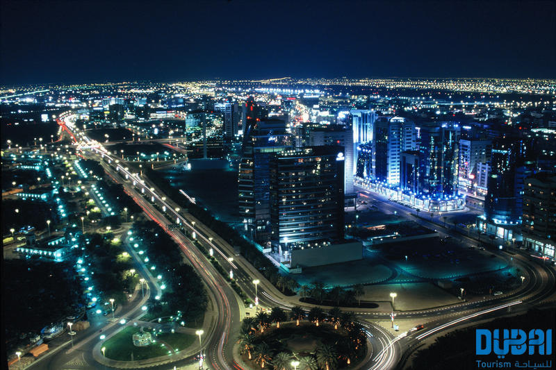 Modern Dubai skyline at sunset with illuminated skyscrapers and a calm waterway.