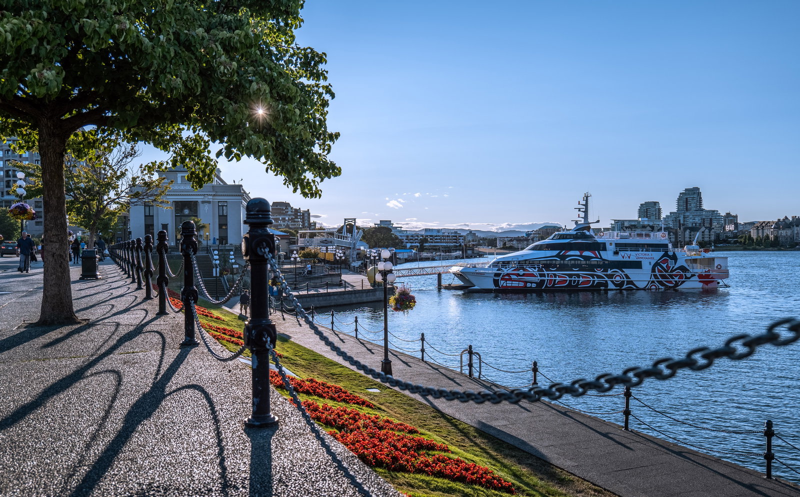 Horse-drawn carriage passing the Parliament Buildings along Victoria's Inner Harbour at sunset.