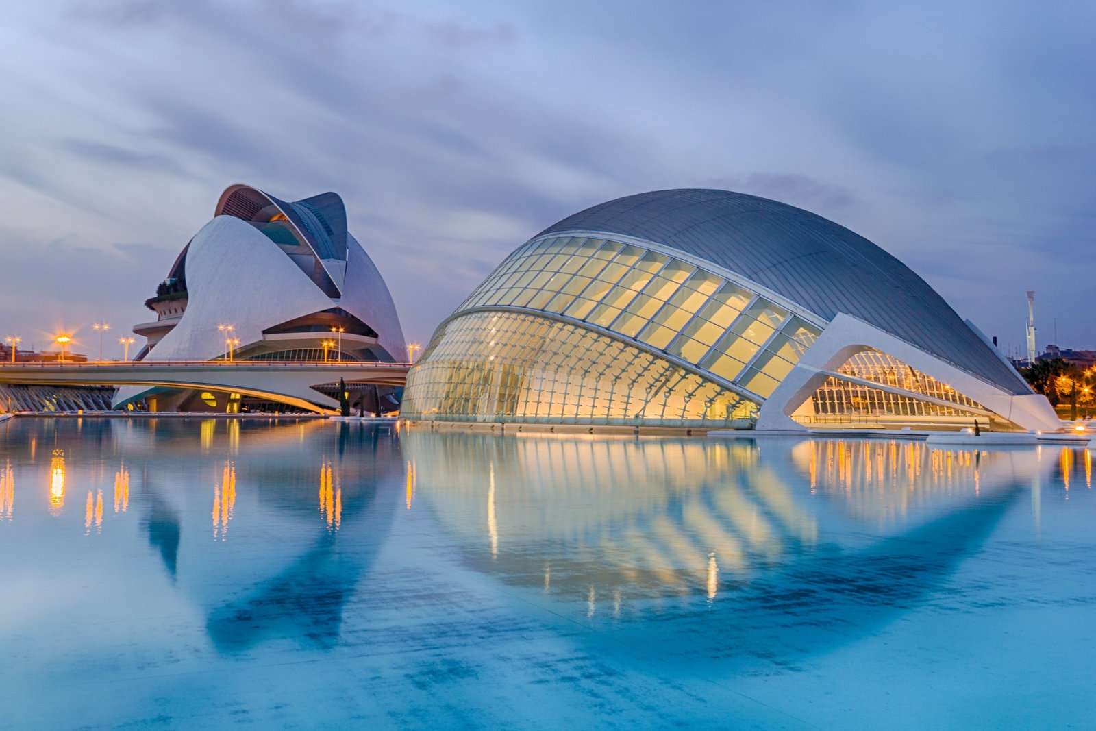 Panoramic view of Valencia's City of Arts and Sciences at sunset, with modern buildings reflected in water.