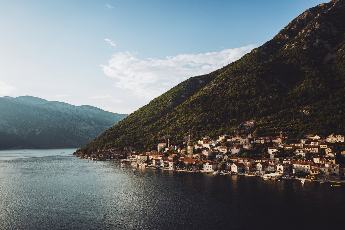 Panoramic view of Kotor's walled Old Town nestled against towering mountains and a calm bay.