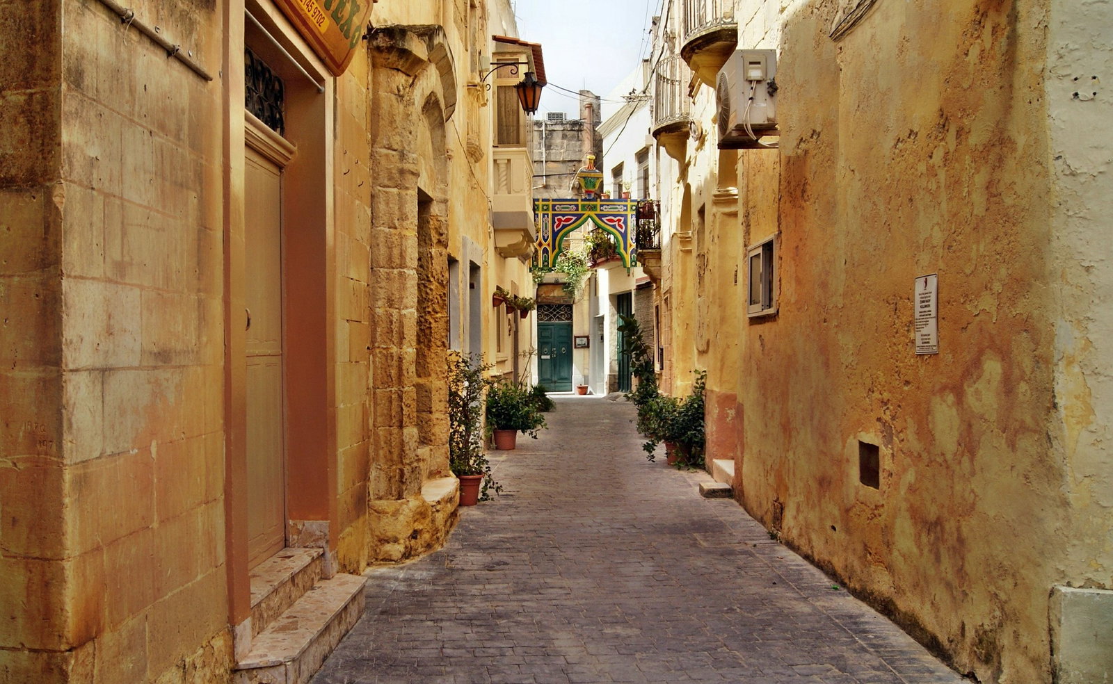 Historic Valletta street with honey-colored stone buildings and traditional wooden balconies.