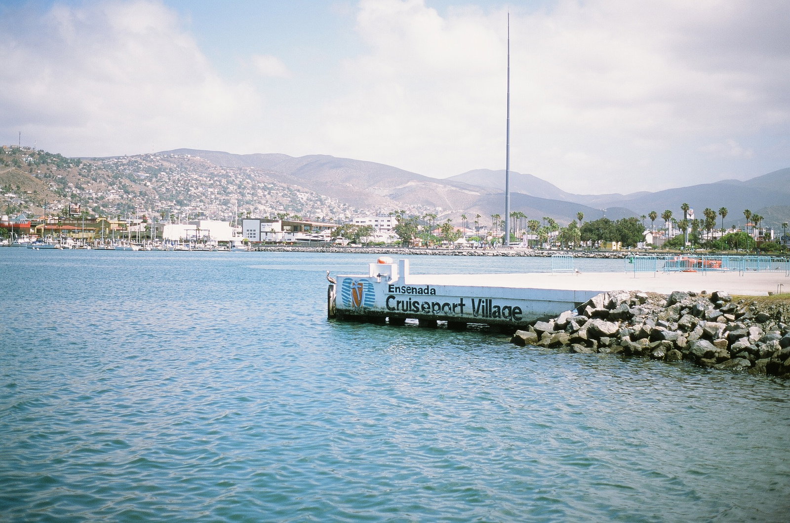 Panoramic view of Ensenada's harbor and waterfront promenade with mountains in the background.