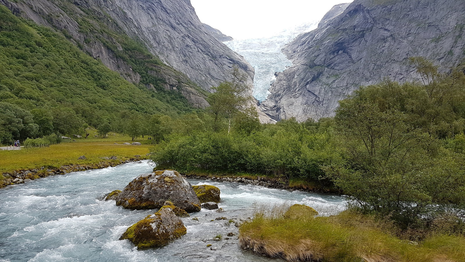 A cruise ship docked in the fjord with a waterfall cascading into the water.