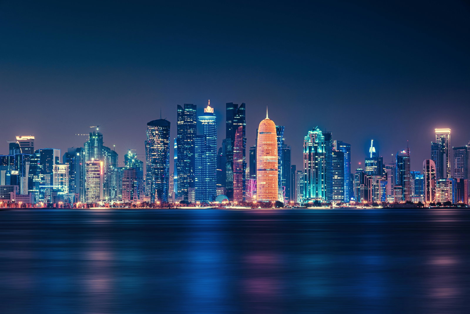 Doha skyline at sunset, with traditional dhow boats in the foreground.