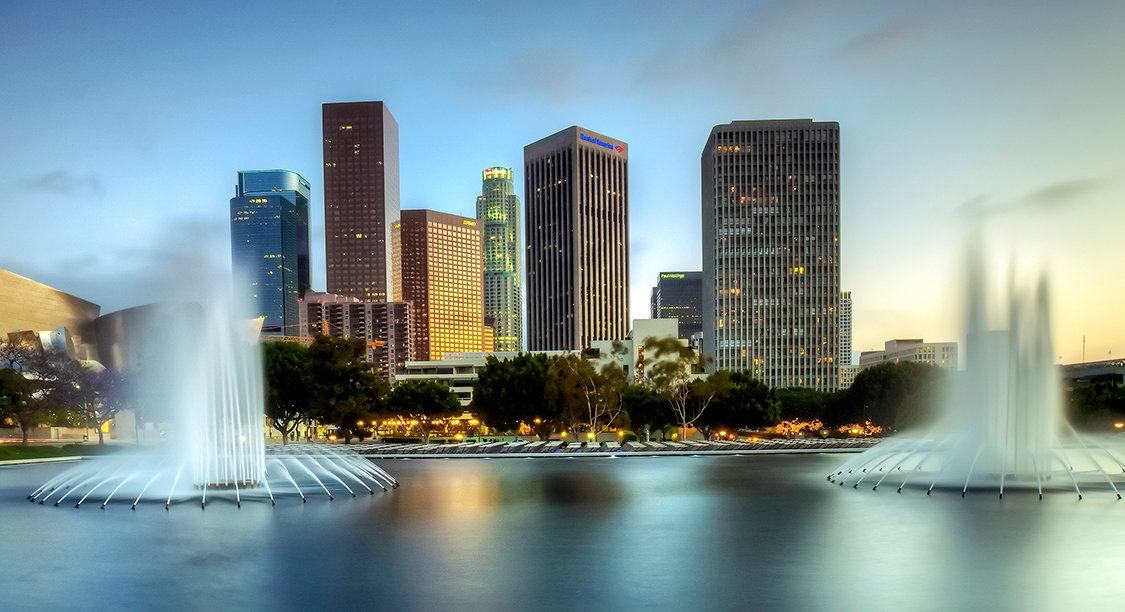 Cruise ship docked at a bustling Los Angeles port with city skyline in background.