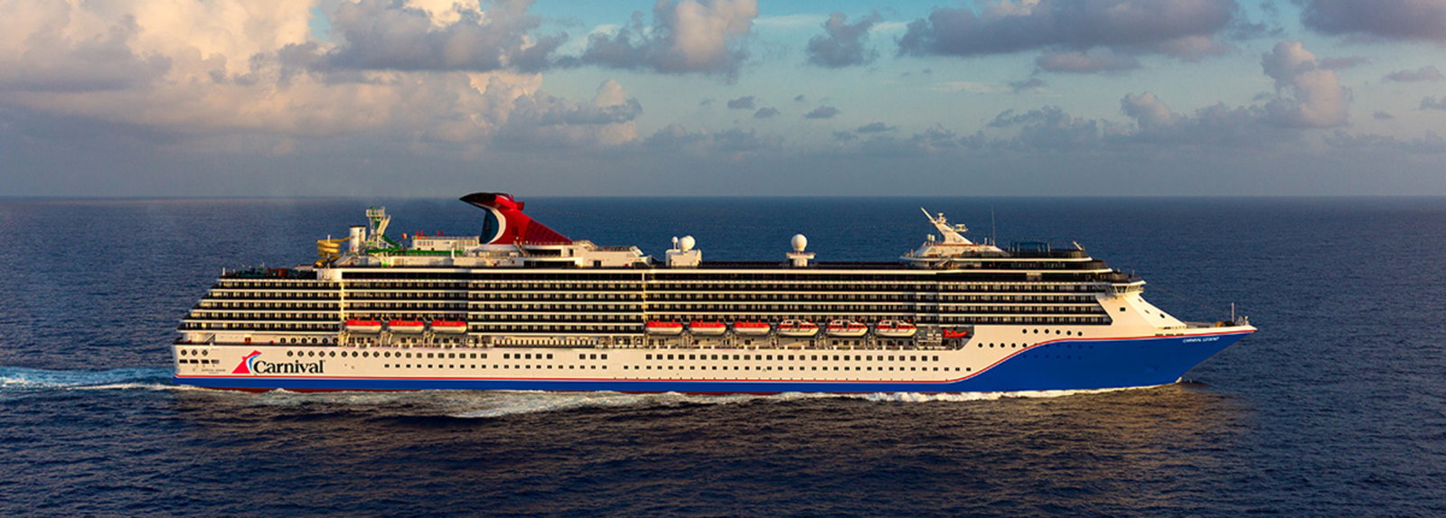 Carnival Legend cruise ship sailing on blue ocean waters at sunset.