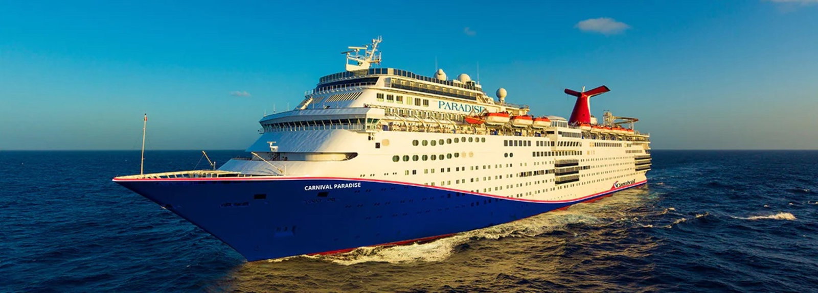 A Carnival Paradise cruise ship sailing on blue ocean waters under a clear sky.