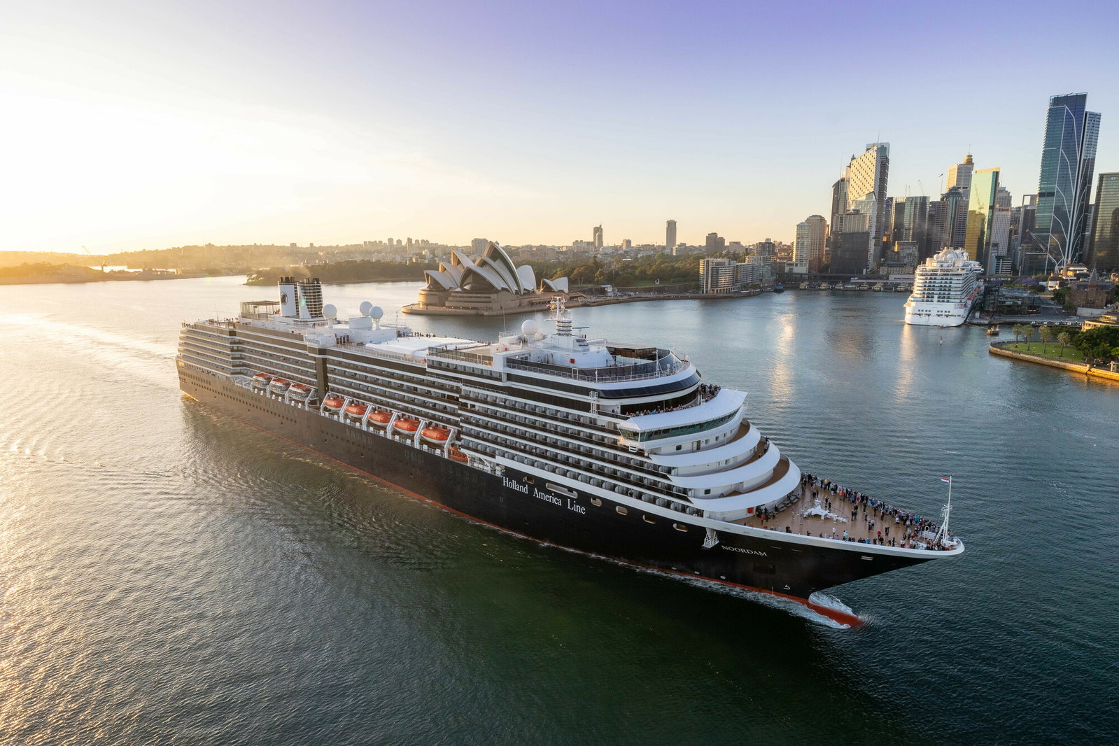 A Holland America Line Noordam cruise ship sailing on calm blue waters.
