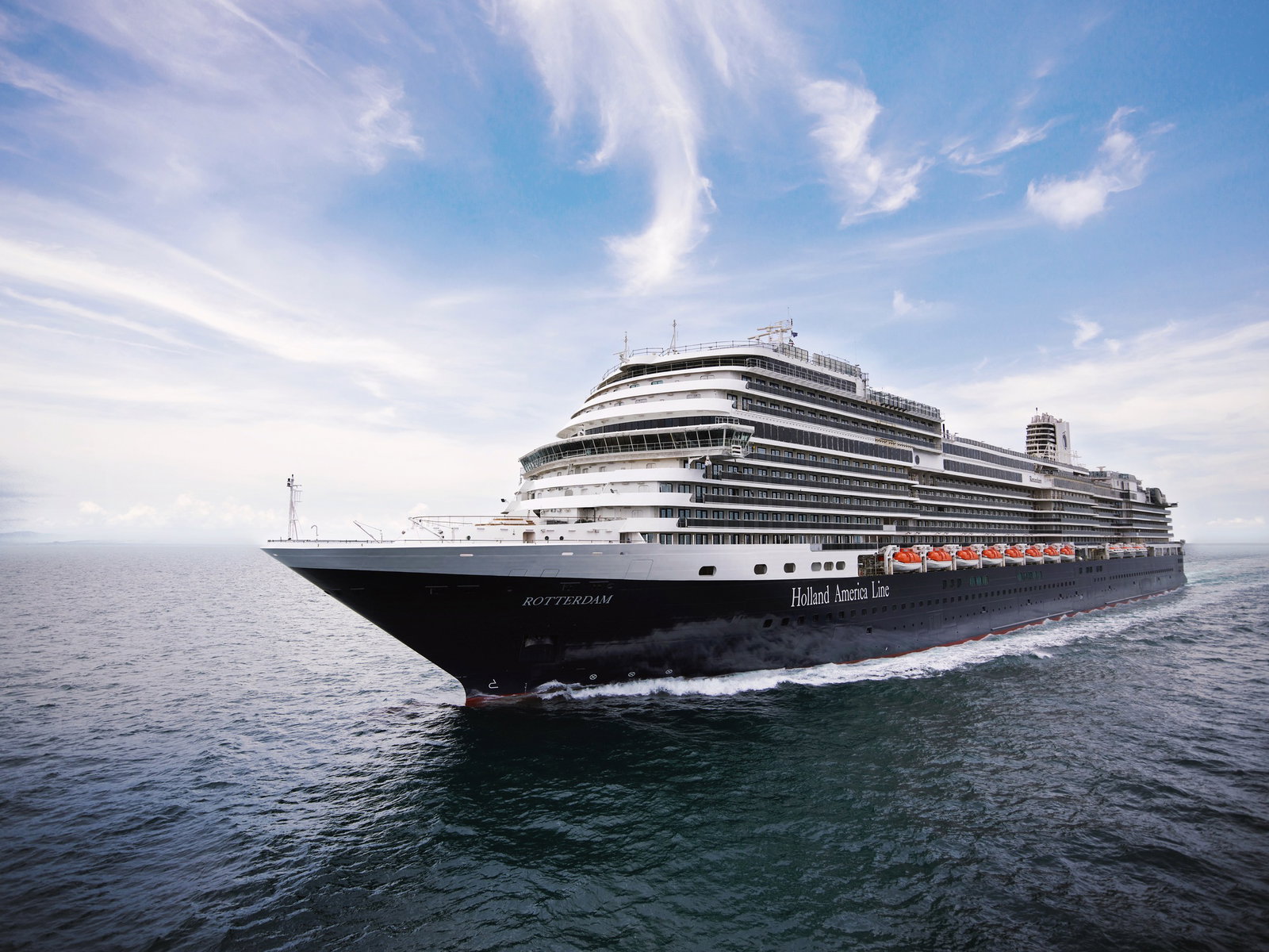 An elegant mid-sized cruise ship, Rotterdam, sailing on calm blue waters under a clear sky.