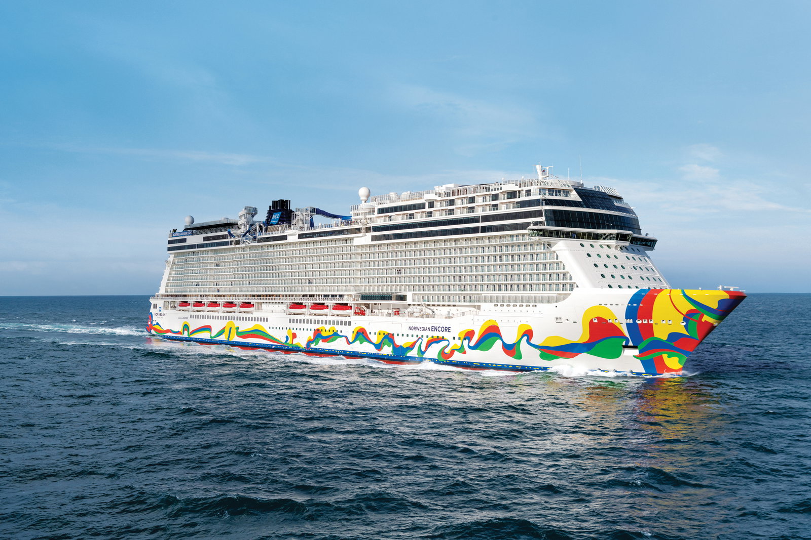 A large cruise ship with a race track on its top deck sailing on blue waters.