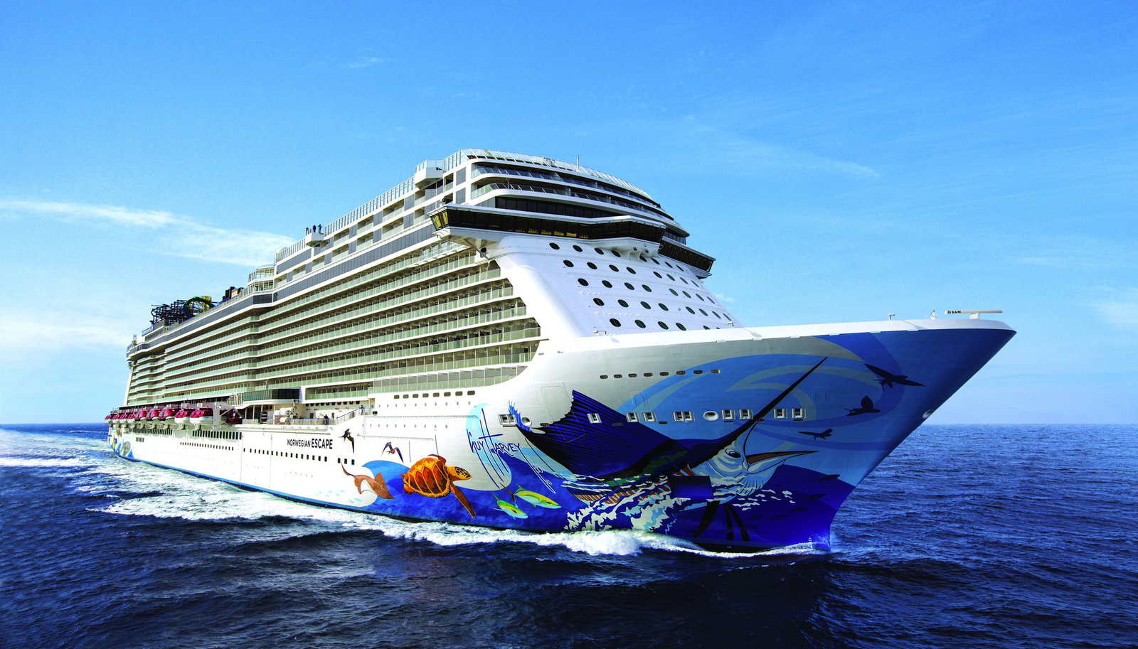 Aerial view of Norwegian Escape sailing on blue ocean waters at sunset.