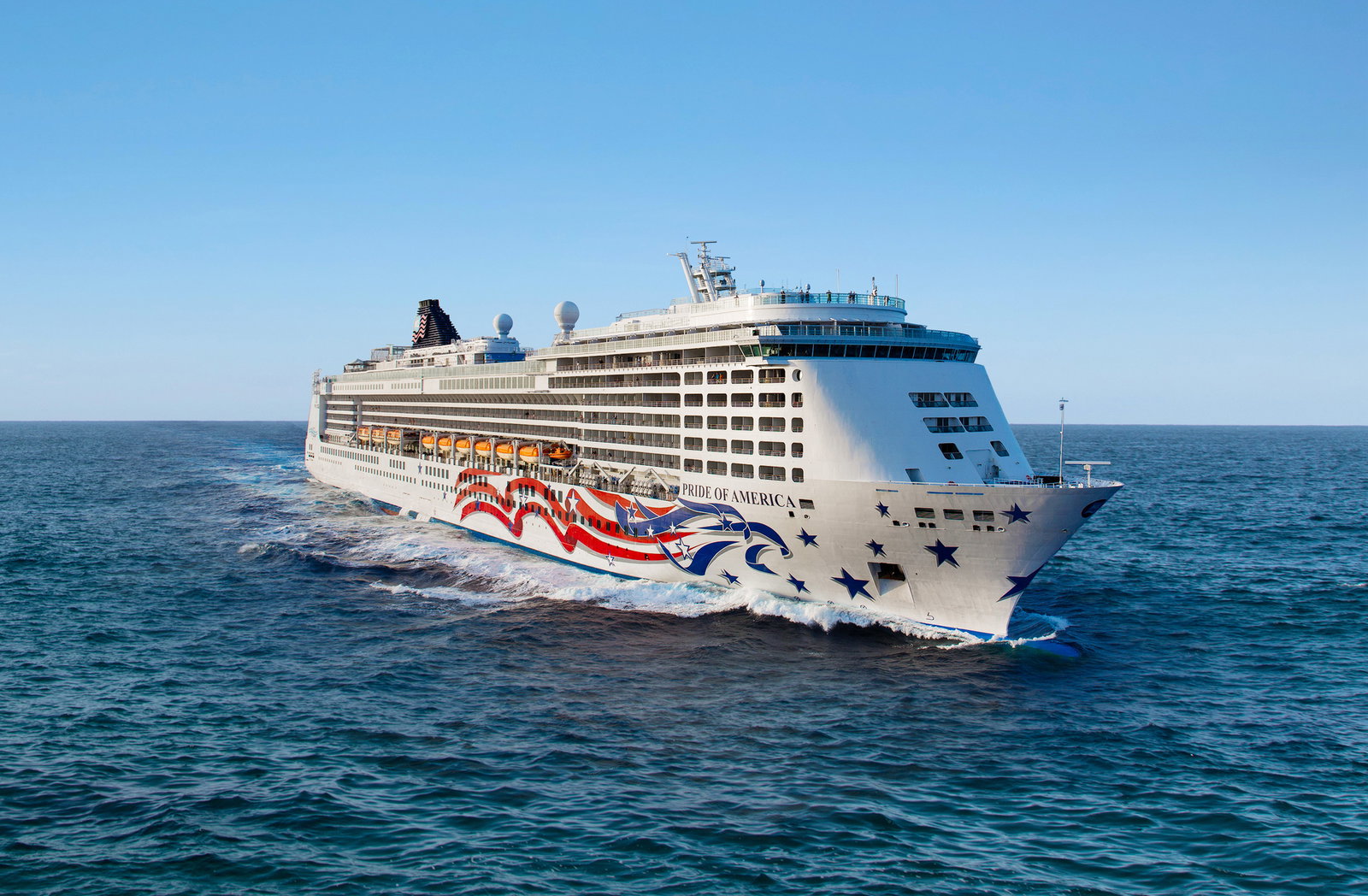 Norwegian Pride of America sailing past lush Hawaiian coastline at sunset.