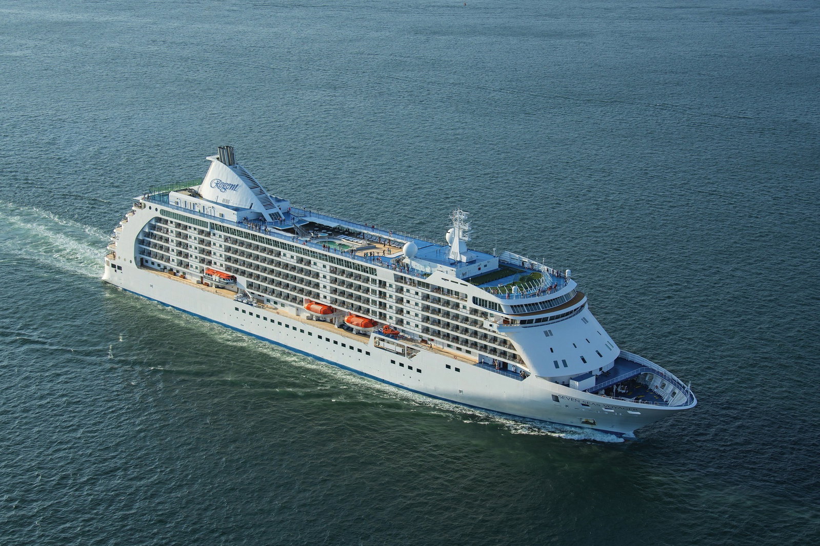 An elegant cruise ship with multiple decks sailing on calm, blue ocean waters.