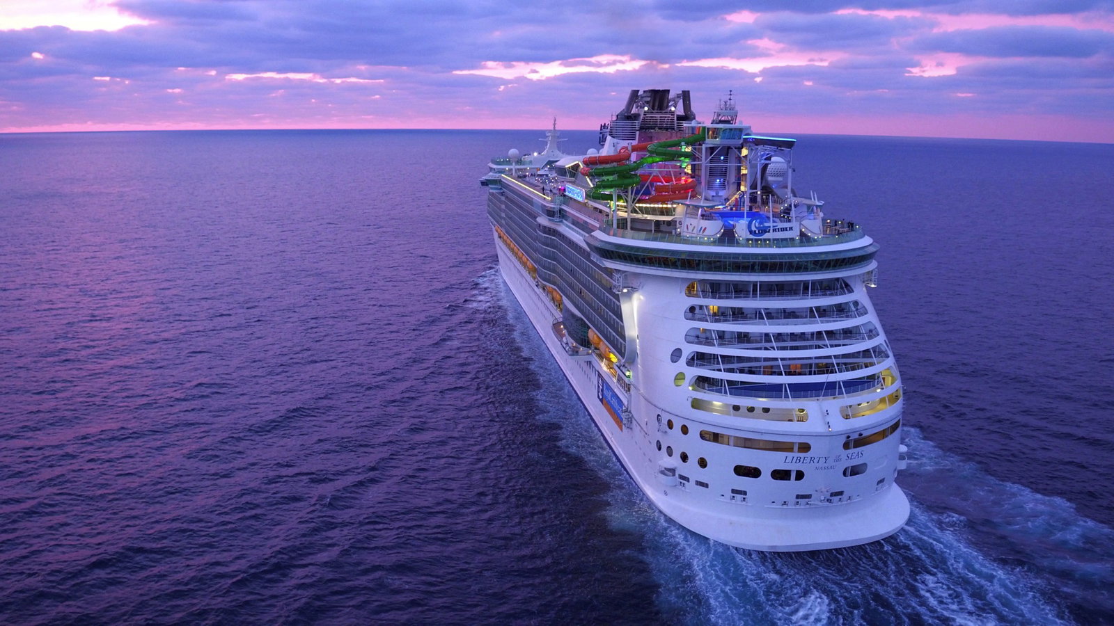 Large Royal Caribbean cruise ship sailing on blue ocean waters at sunset.