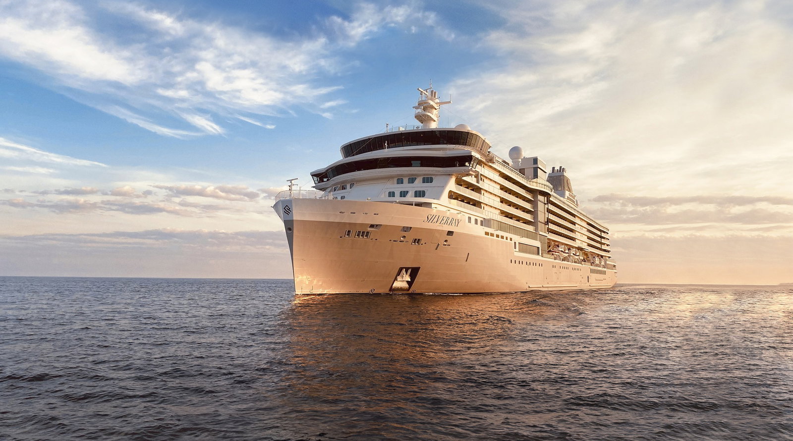 A sleek, small luxury cruise ship navigating a pristine, remote bay under clear skies.