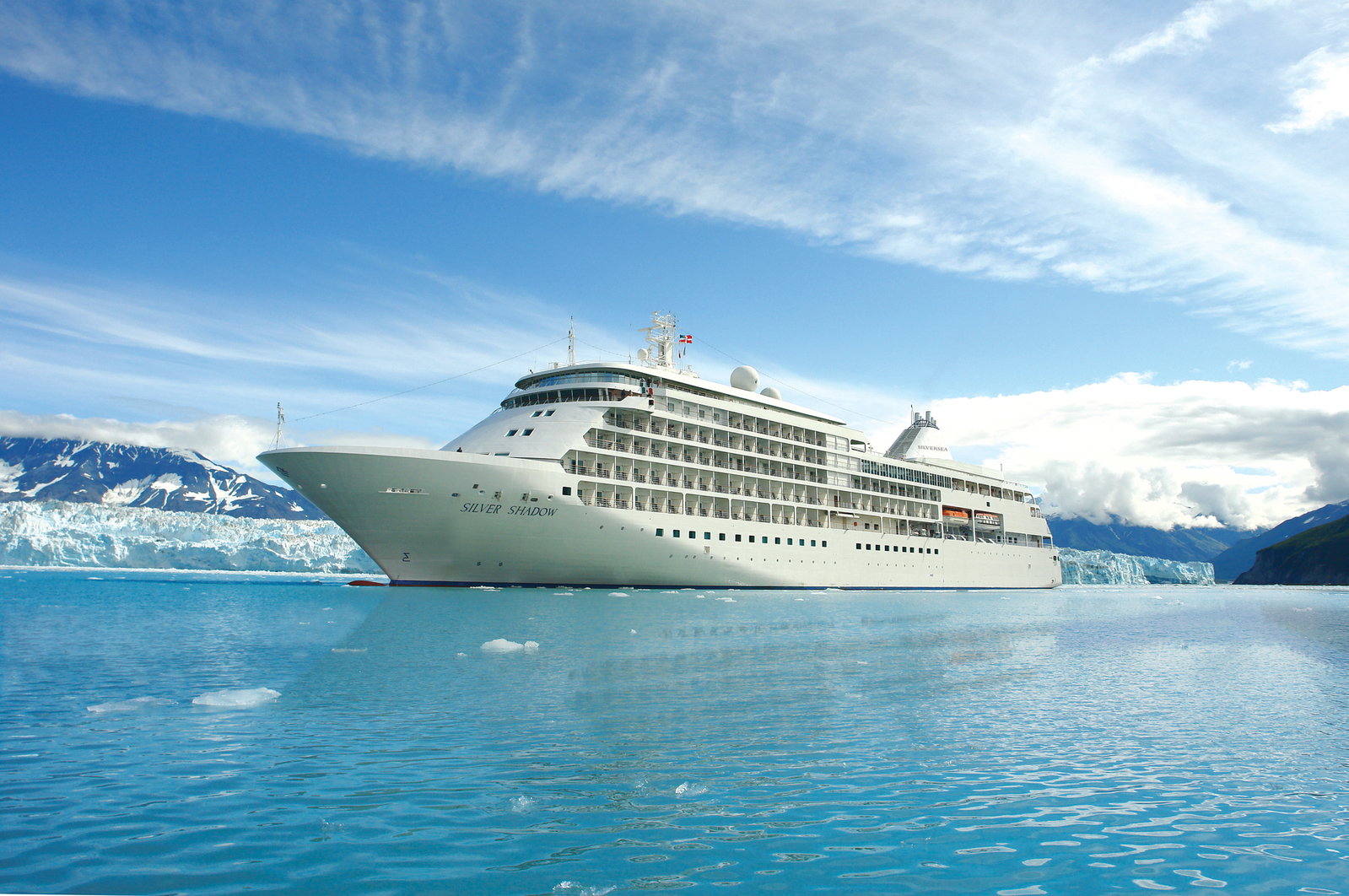 A luxurious cruise ship sailing on calm waters with a clear sky, viewed from the side.