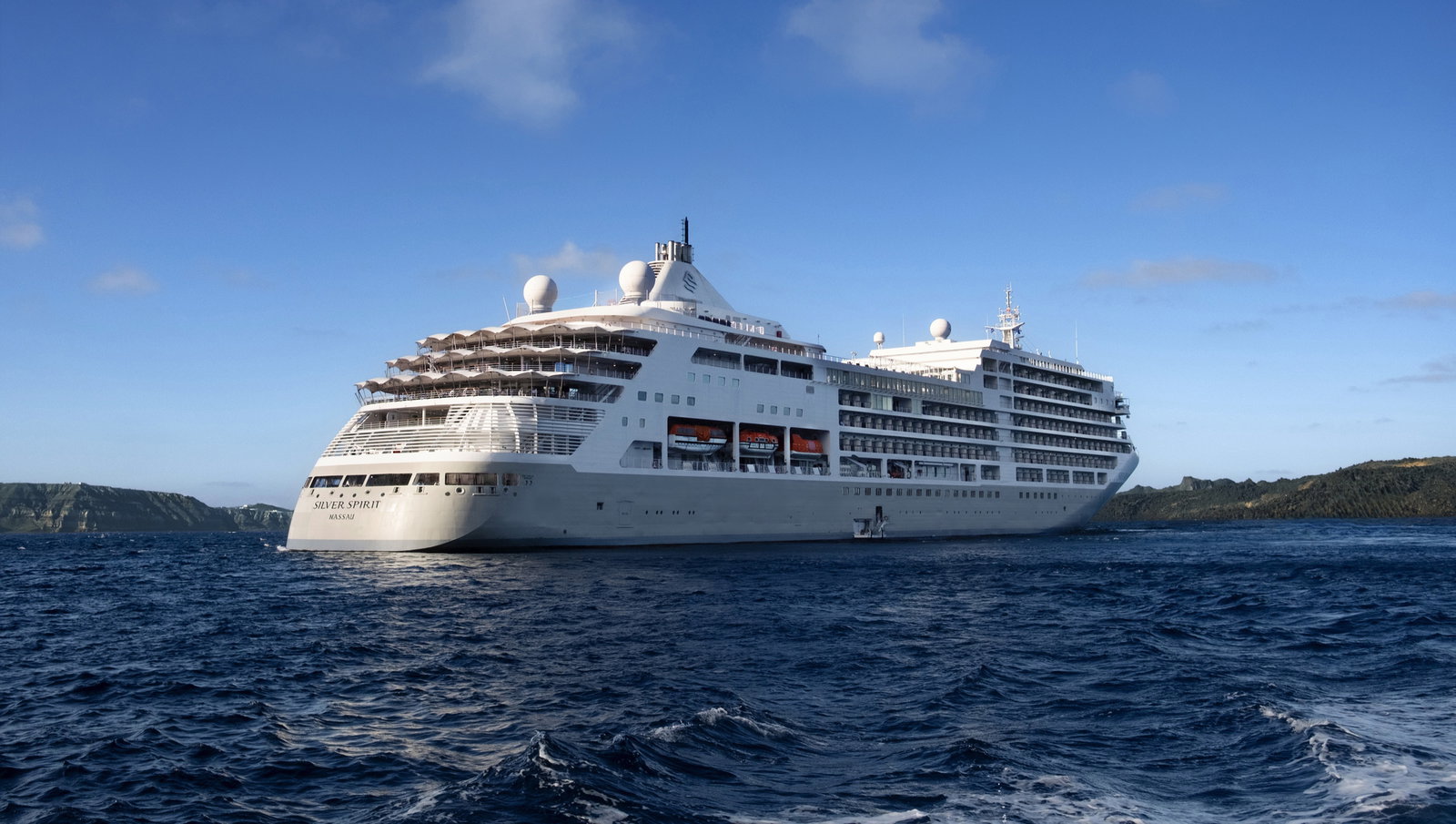 A luxurious cruise ship sailing on calm waters at sunset, with lights illuminating its decks.