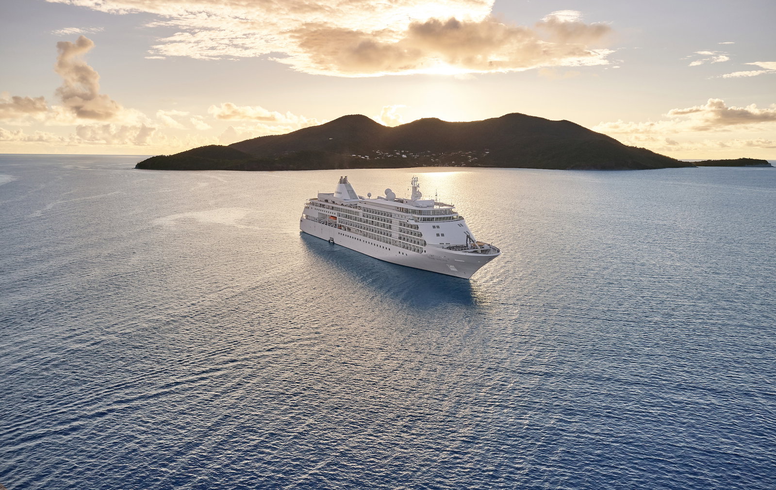 An elegant luxury cruise ship sailing on calm waters at sunset.